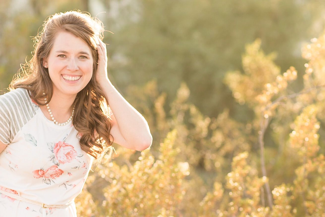 Woman in floral top poses in golden field during sunset.