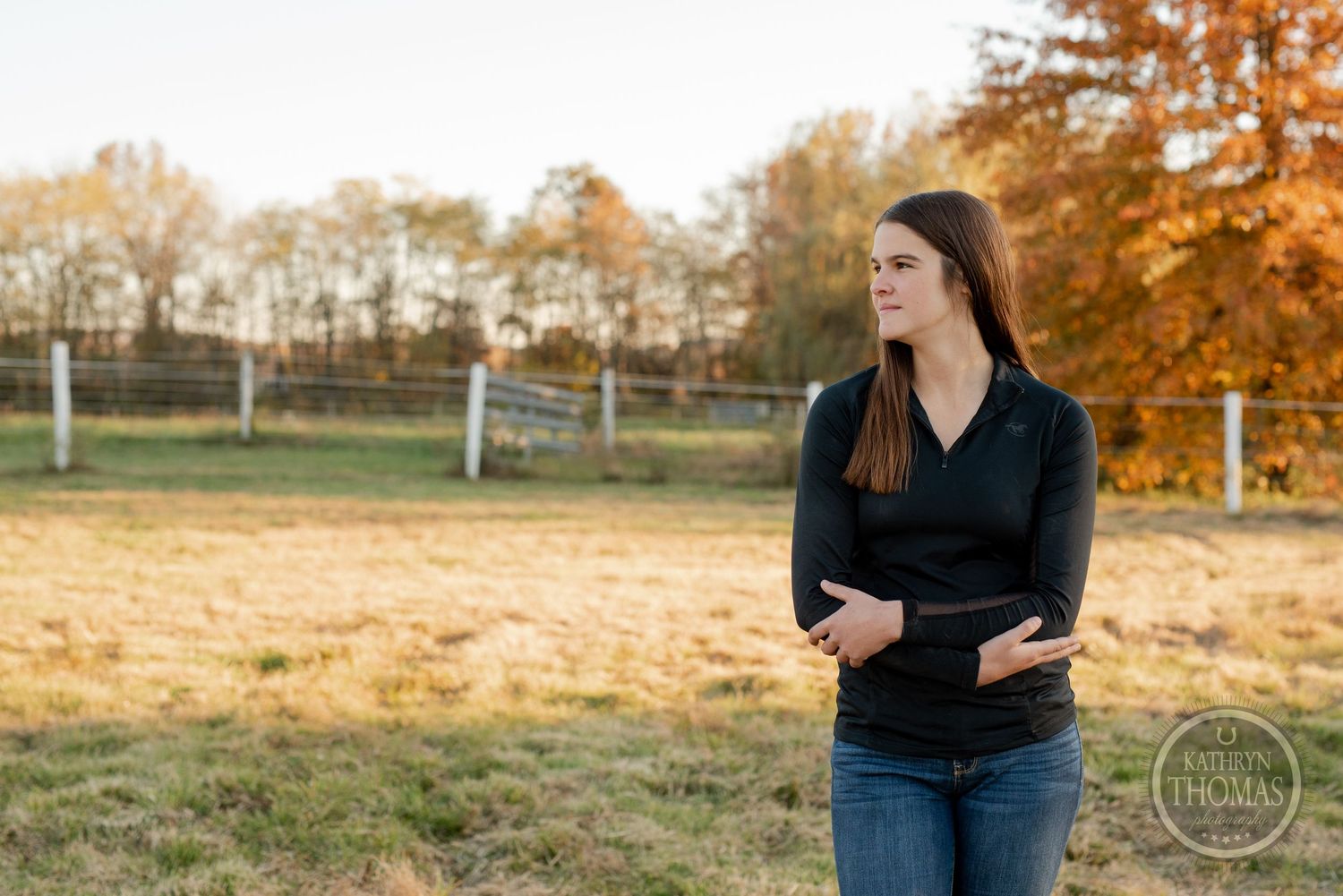 Casual outdoor portrait against autumn trees and fencing in golden afternoon light.