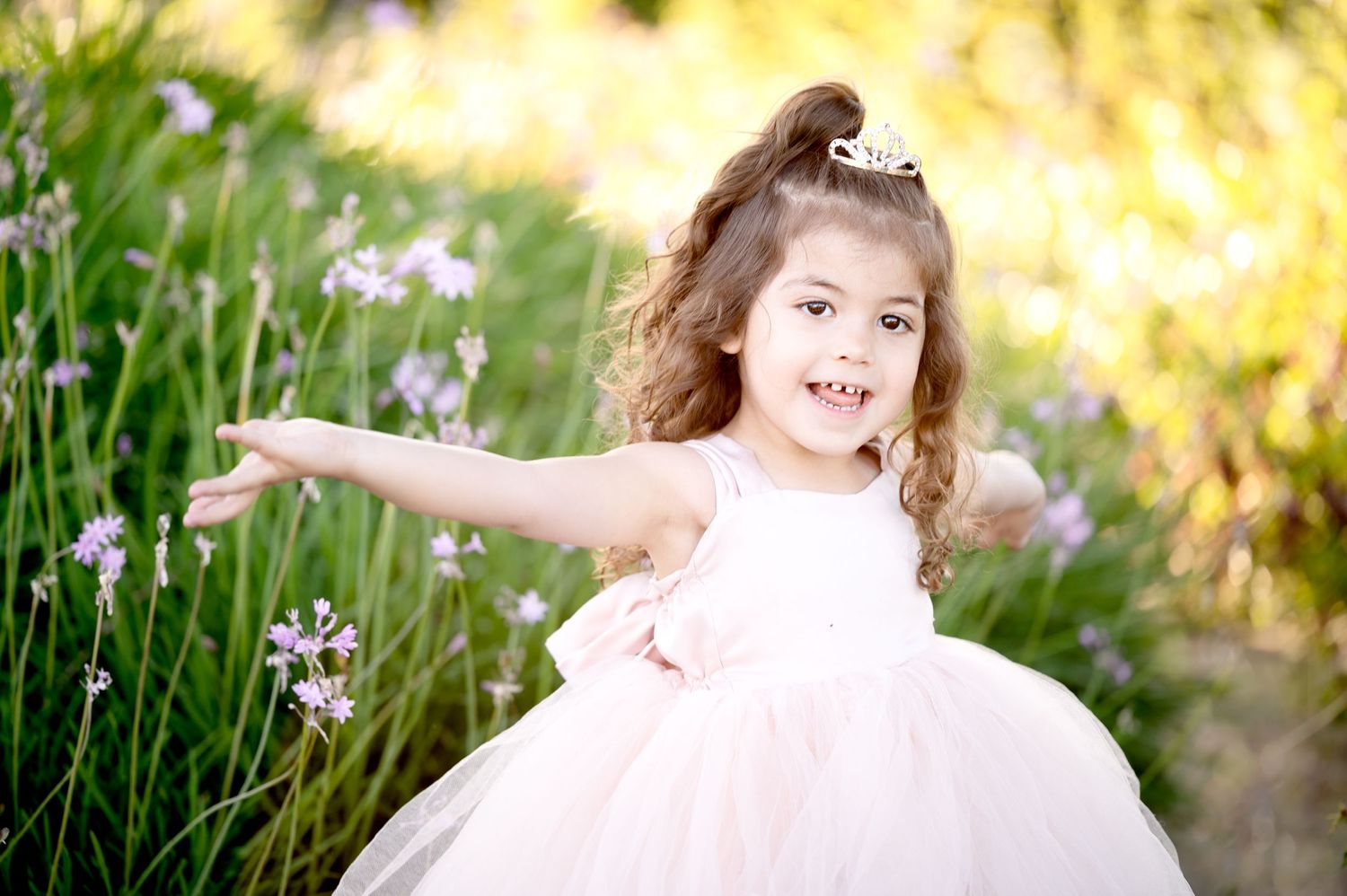 Child in pink princess dress twirling in garden with golden sunset lighting.