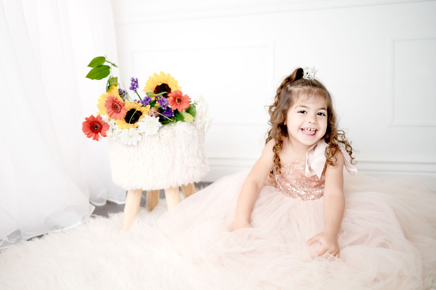 A joyful indoor portrait with a white backdrop and colorful floral arrangement.