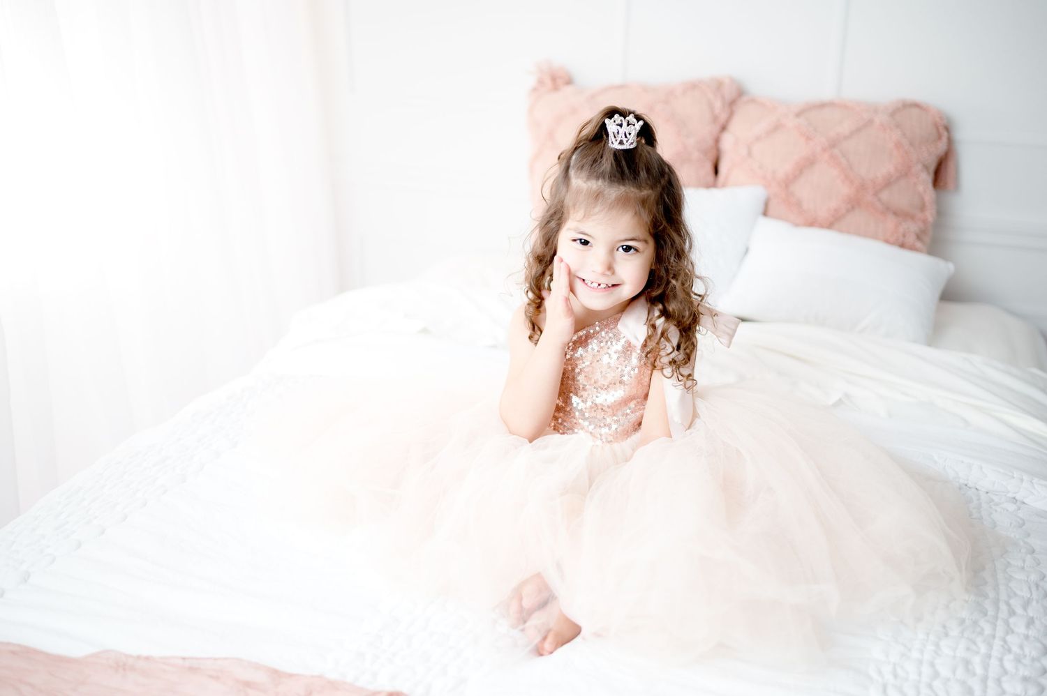 A sweet princess-inspired portrait on white bedding with soft pink accents.