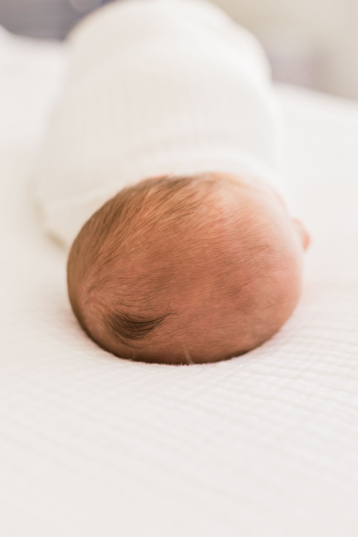 Close up view of a sleeping baby's head against white bedding.