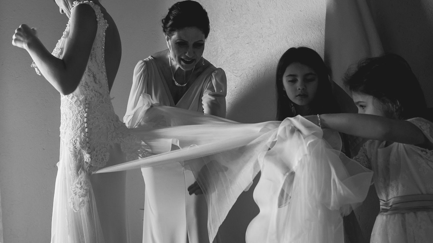 A black and white image showing wedding dress preparations with helpers adjusting the gown.
