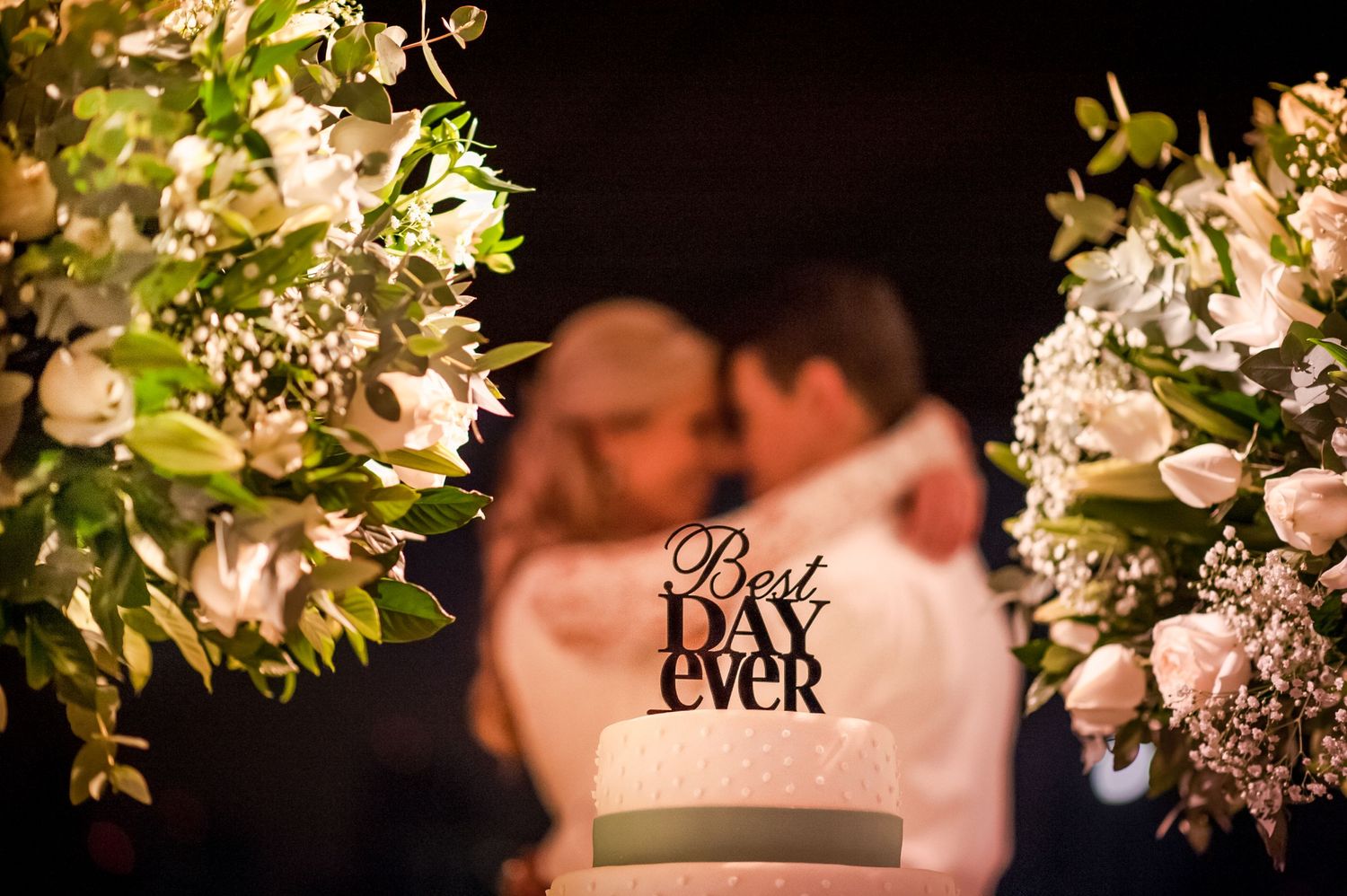 Best Ever cake topper with white floral arrangements framing a soft focus romantic scene.