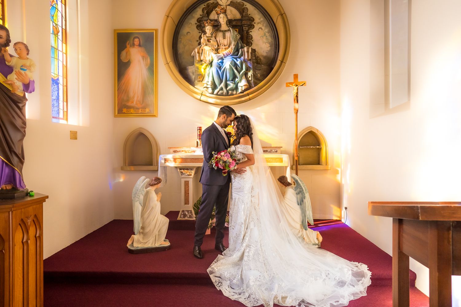 A wedding couple stands before an ornate church altar with religious artwork and stained glass windows.