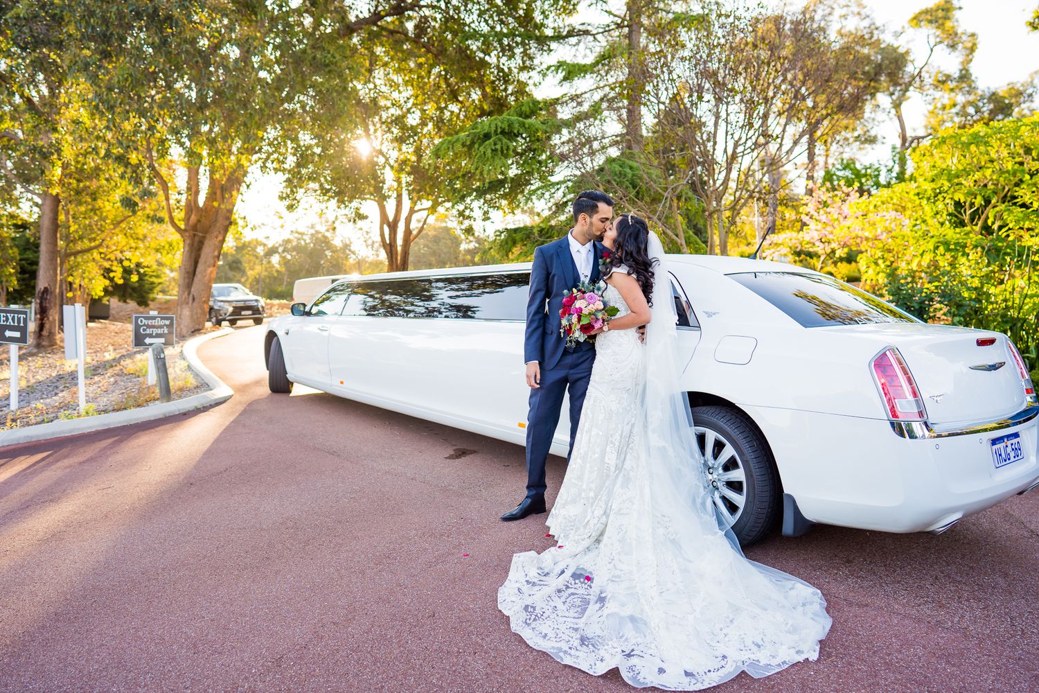 A white stretch limousine parked on a tree-lined path during golden hour.