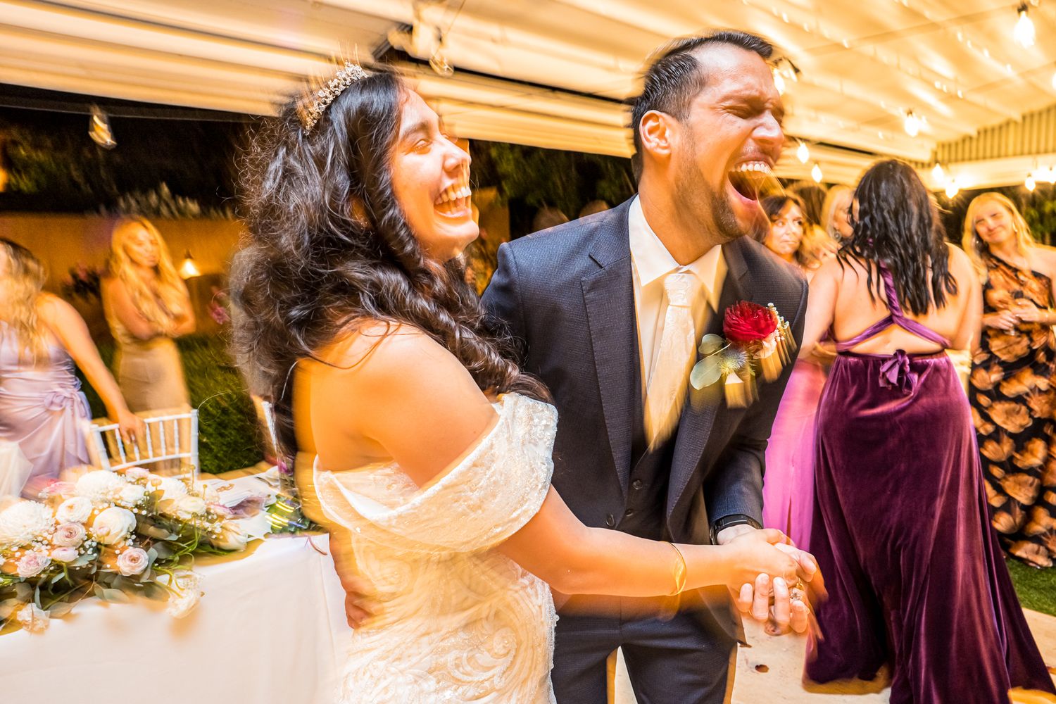 A couple laughs together on their wedding day during a lively reception.