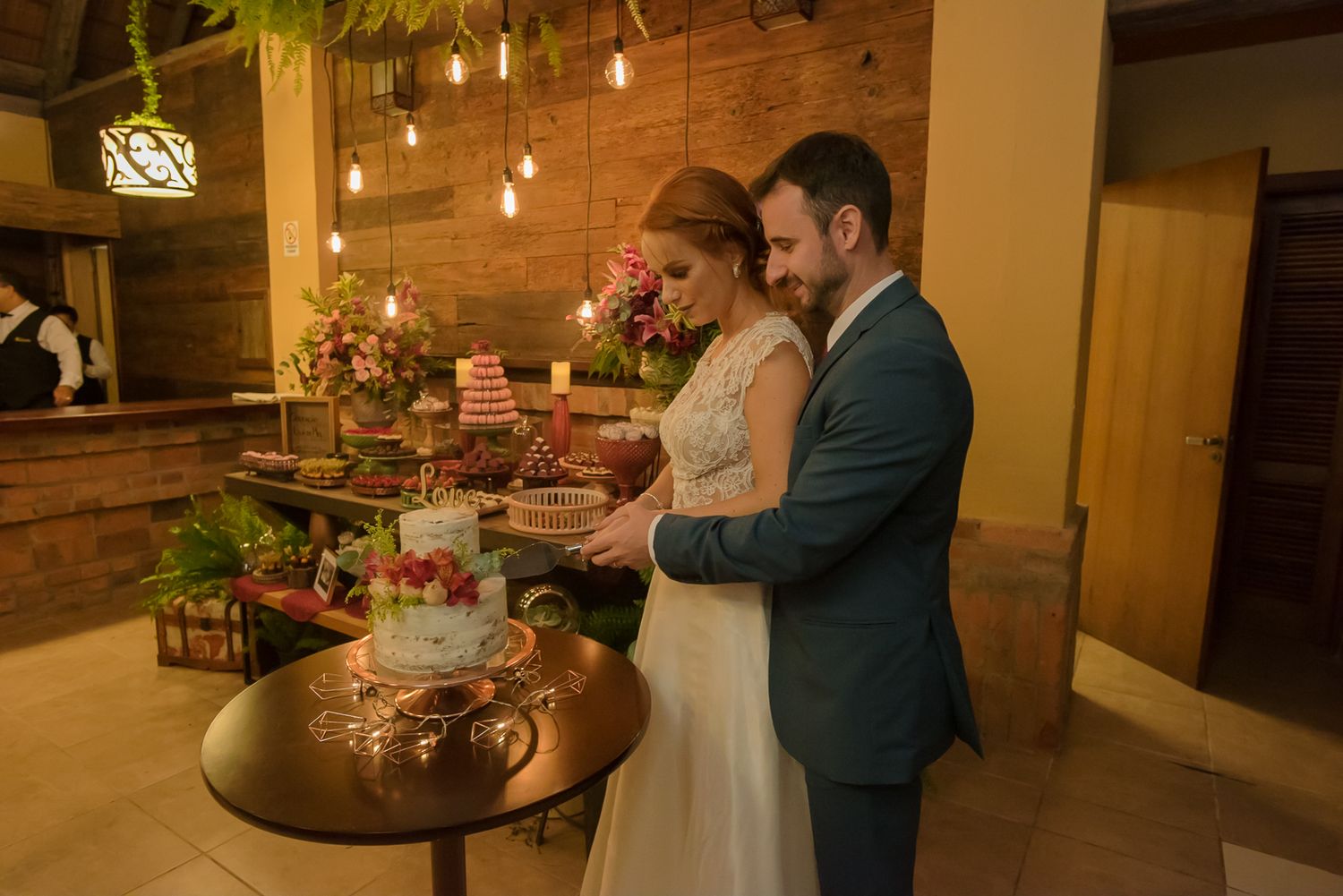 Warm-lit reception scene with rustic wood walls and dessert table.
