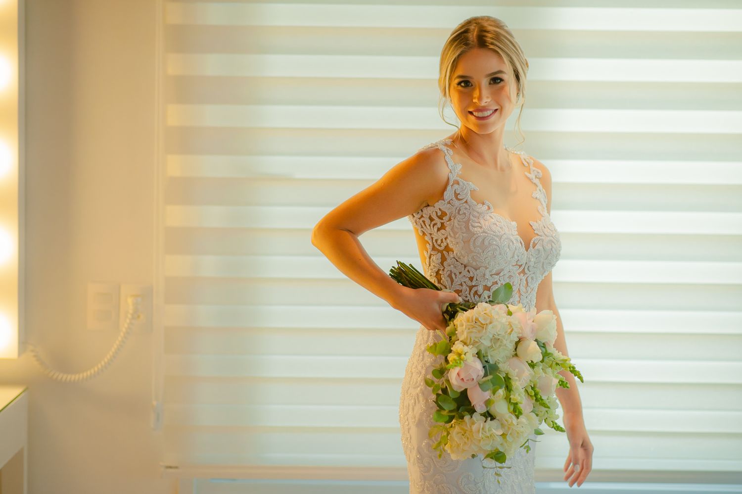 Bride in elegant lace gown poses against striped background.