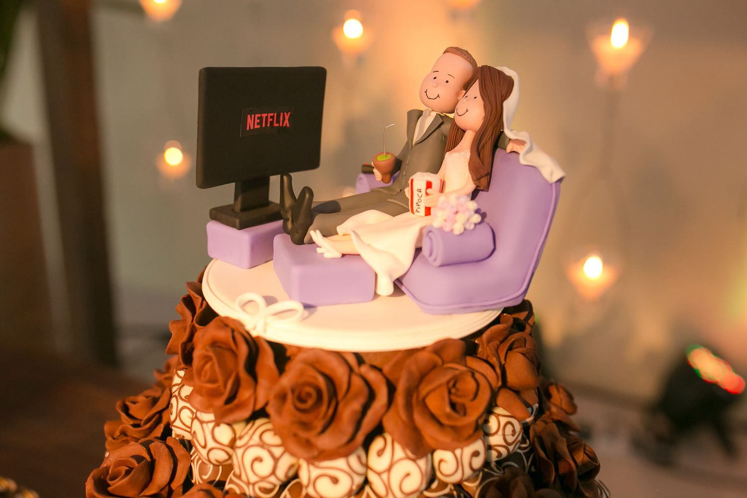 A decorative wedding cake topper featuring a Netflix theme with miniature figures and soft lighting.