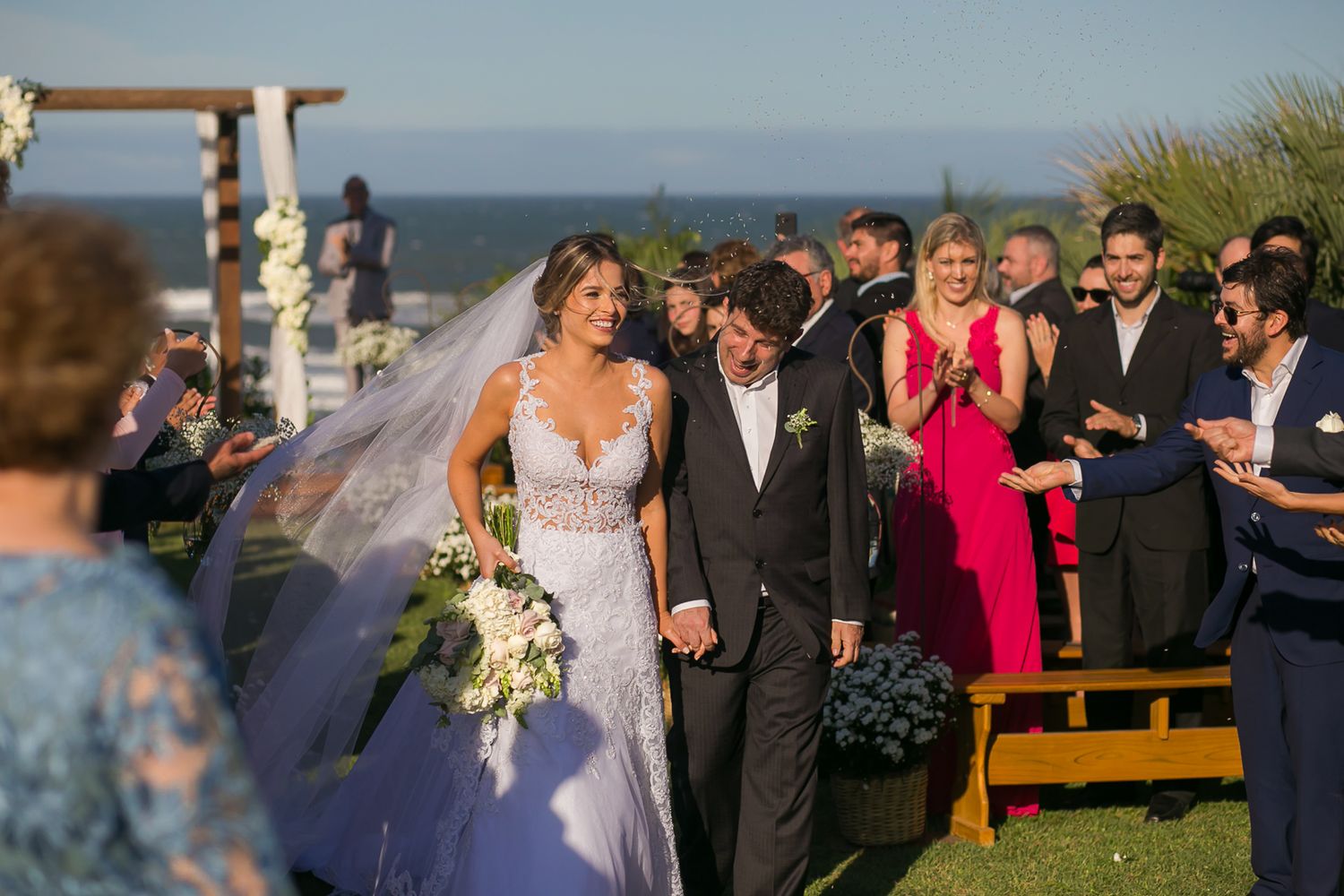 A wedding ceremony taking place on an oceanfront lawn with guests and decorative floral arrangements.