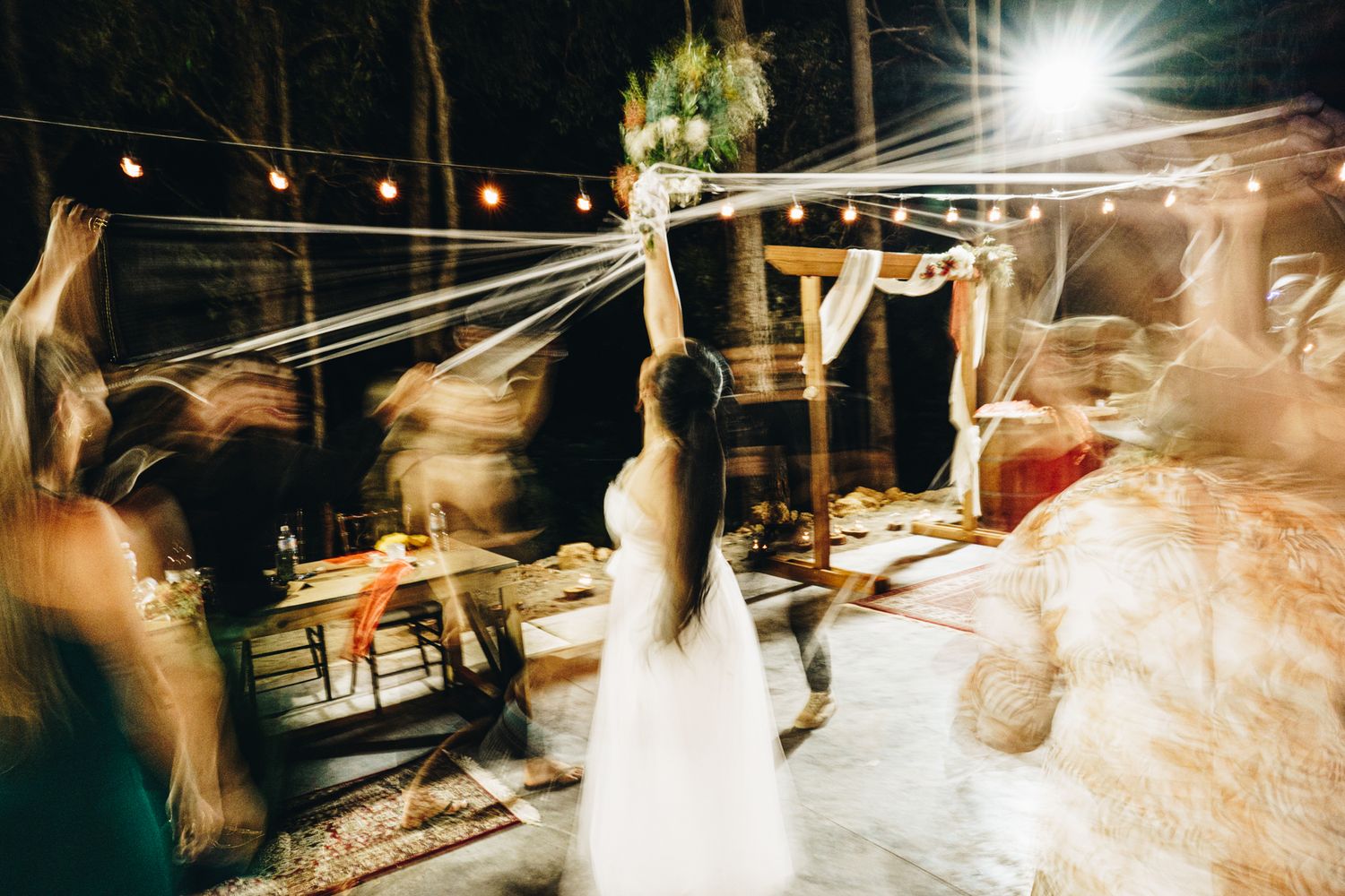 Blurred motion wedding dance under string lights at outdoor reception venue.