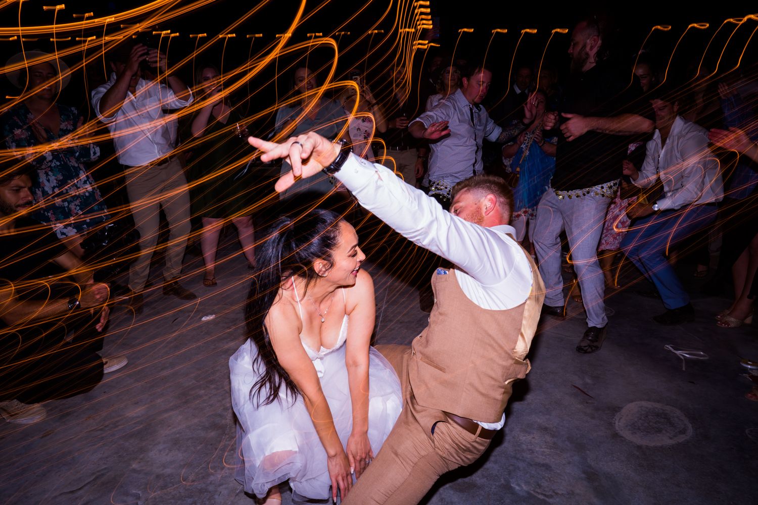 Couple dancing energetically at wedding reception with motion blur and string lights.