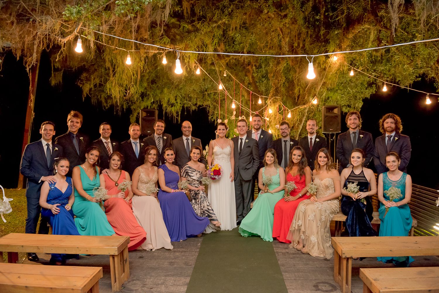Wedding party poses outdoors under string lights at evening ceremony.