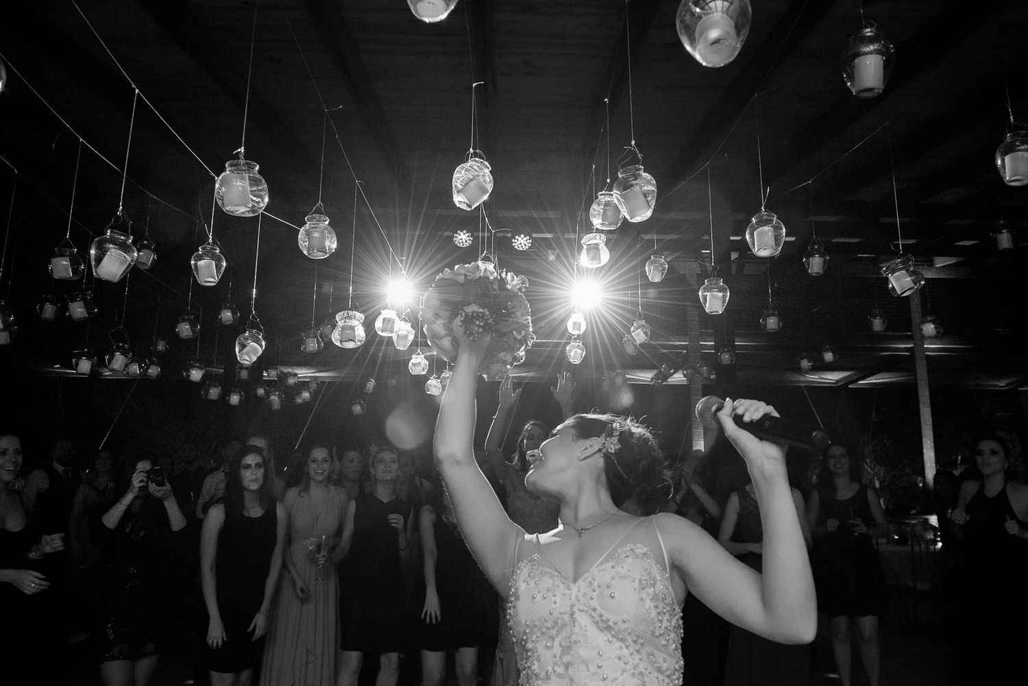 Woman in formal dress singing under hanging lights at wedding reception.