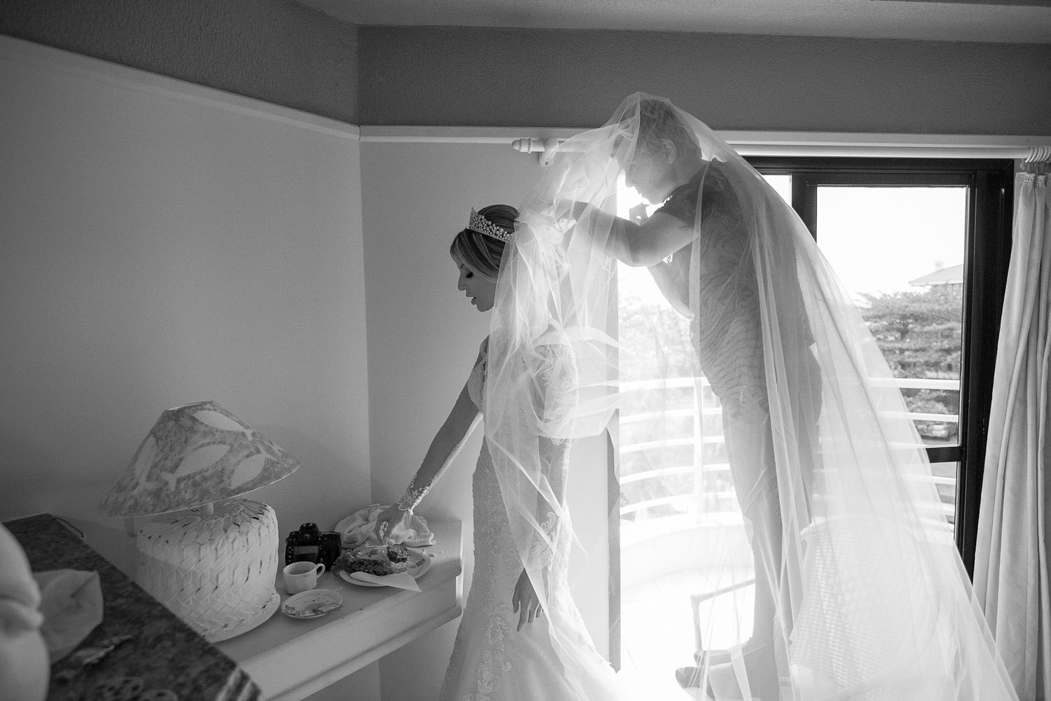 A flowing white wedding dress and veil captured in dramatic window light.