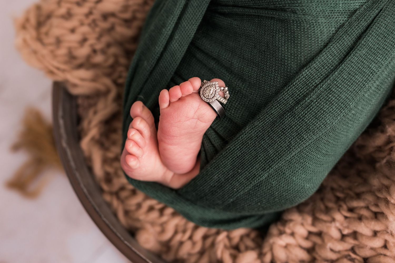 Close-up of newborn baby feet peeking from green wrap with tiny ring, resting on knit blanket.