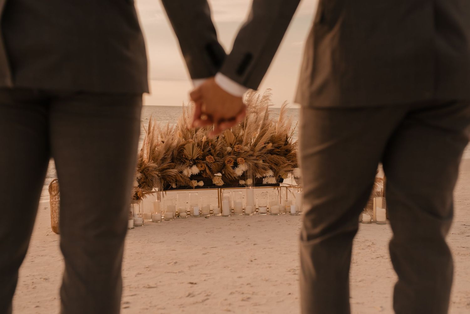 Close up shot of two people holding hands with dried flowers during sunset.