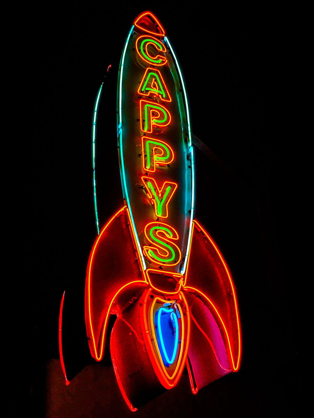 Vintage neon rocket ship sign glowing in red and green against black background.