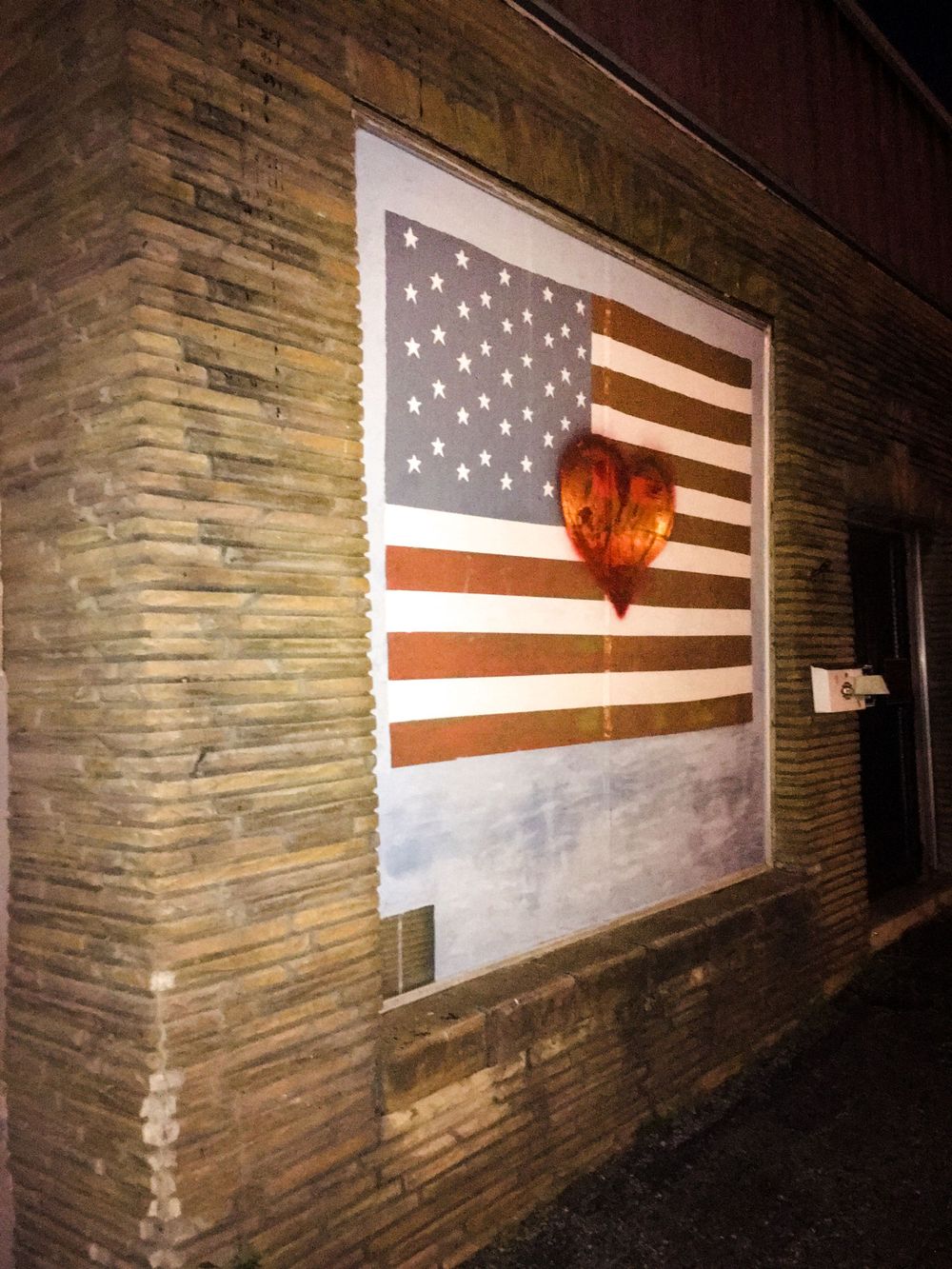 American flag painted on a brick wall illuminated by glowing light in a darkening walkway.