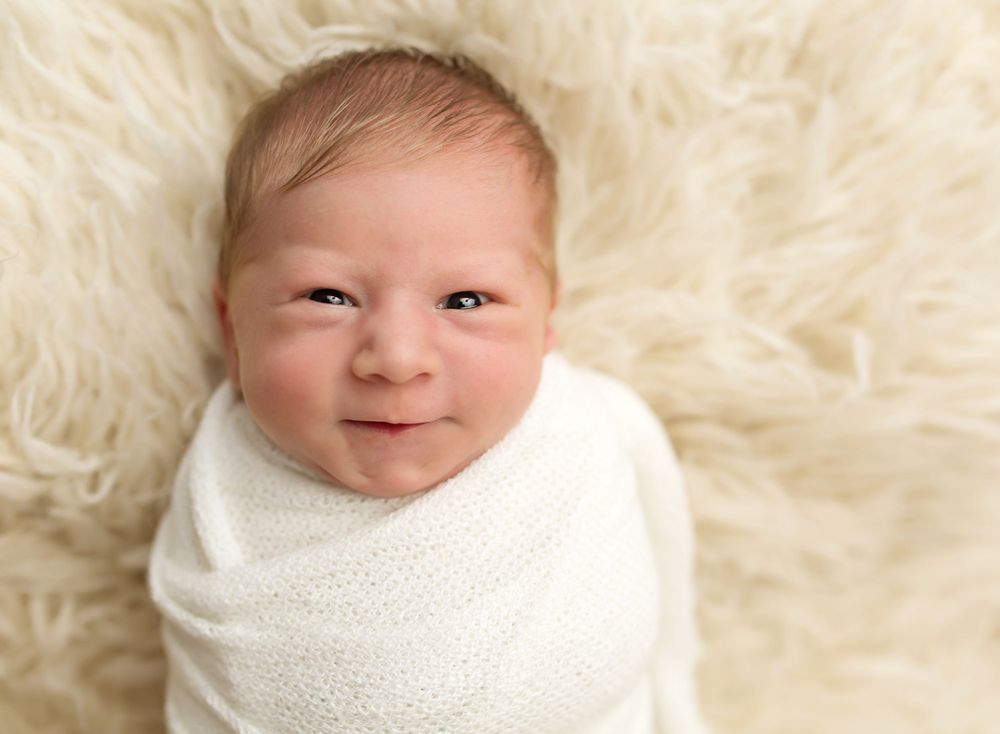 Newborn wrapped in white blanket on fluffy sheepskin background.