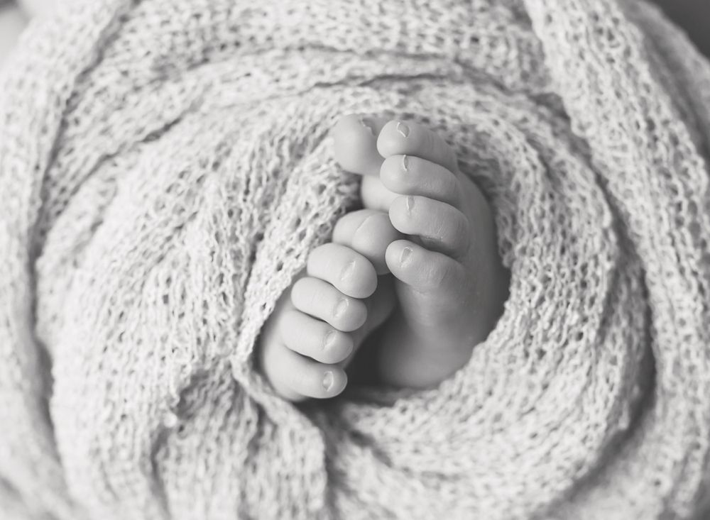 Close-up black and white photo of tiny baby toes wrapped in soft textured blanket.
