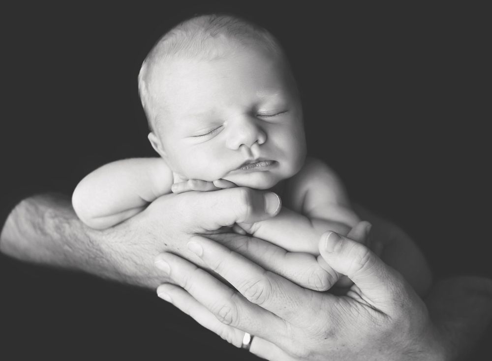 Black and white portrait of sleeping baby cradled in gentle hands.