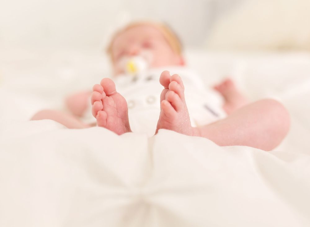 Soft focus photo of baby feet against white bedding.