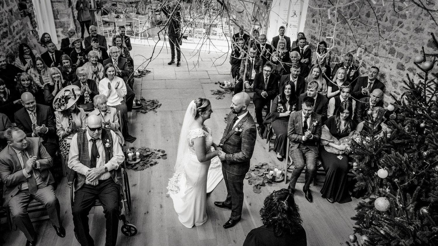 Black and white photo of a wedding ceremony in a stone-walled venue with gathered guests.
