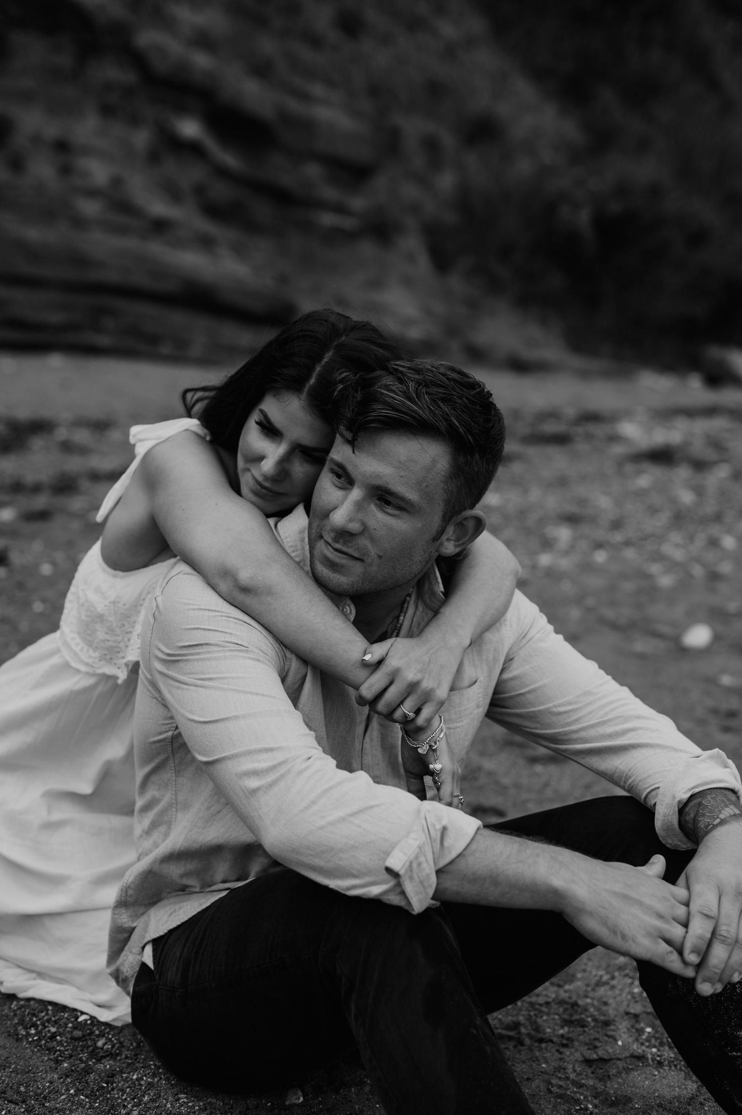 Black and white romantic portrait of a couple embracing outdoors in casual white clothing.
