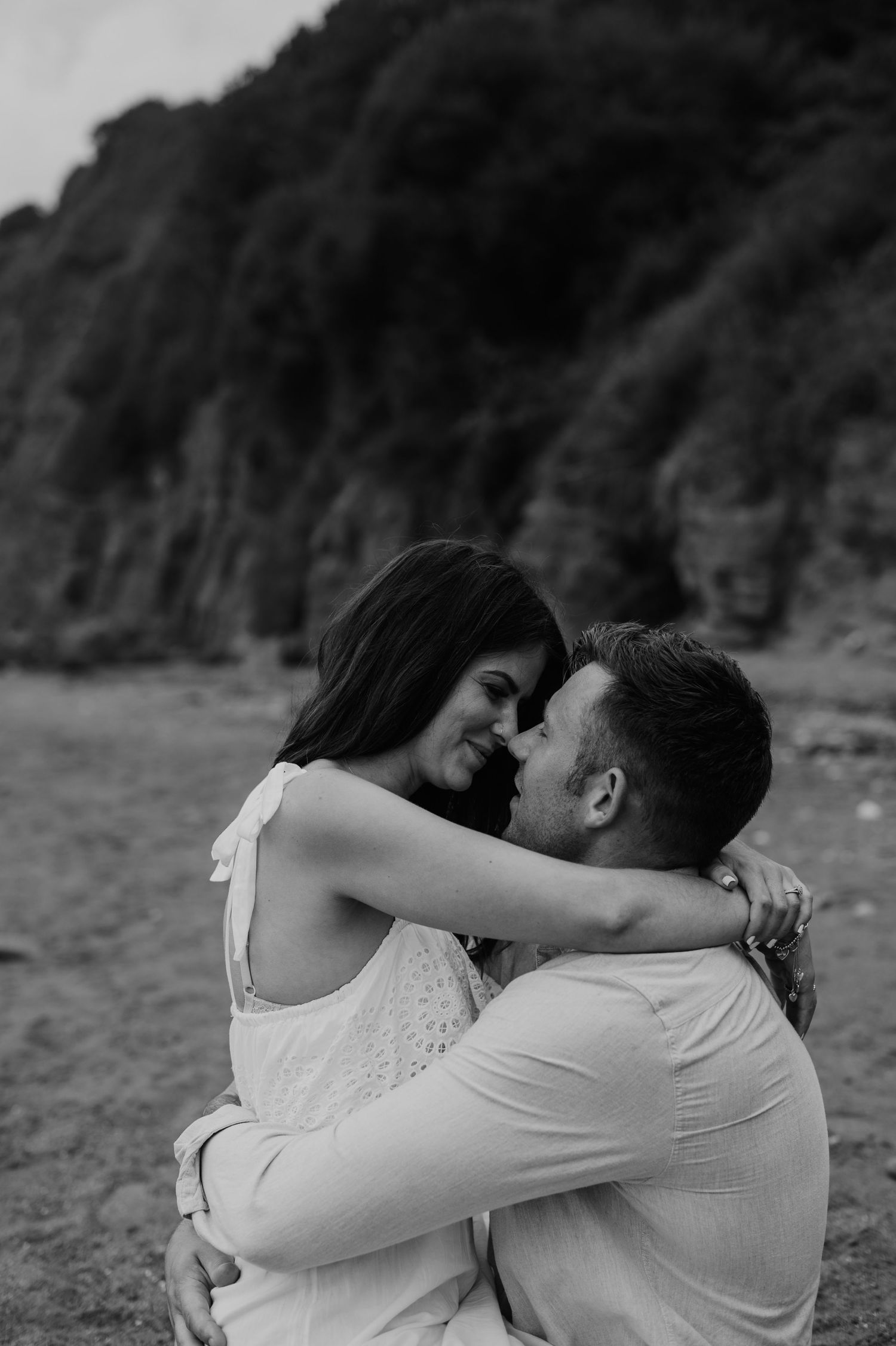 A romantic black and white photo of a couple embracing outdoors against a rocky cliff background.