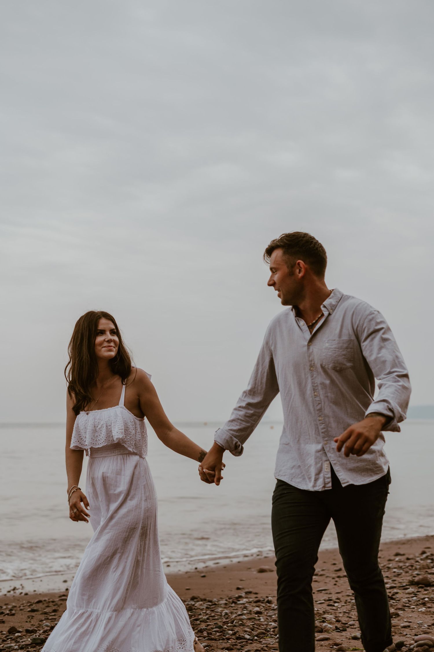 Happy couple playfully run barefoot on the stunning Shaldon beach.