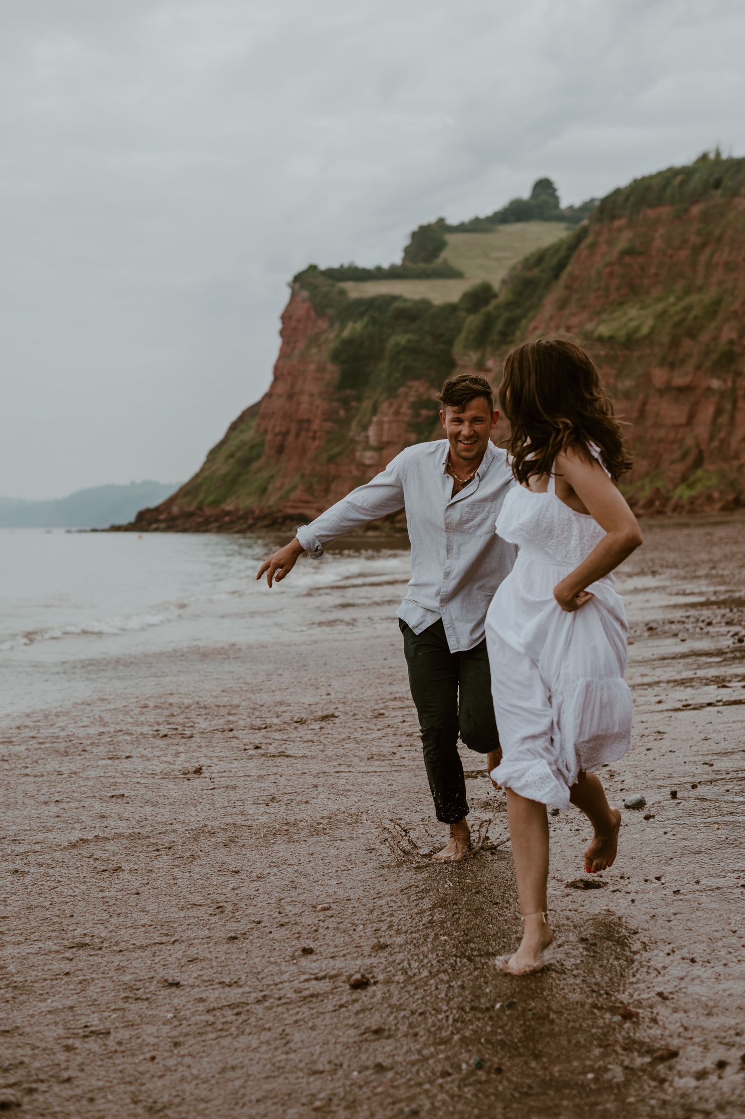 Couple running on the beach at their engagement shoot in Teignmouth.
