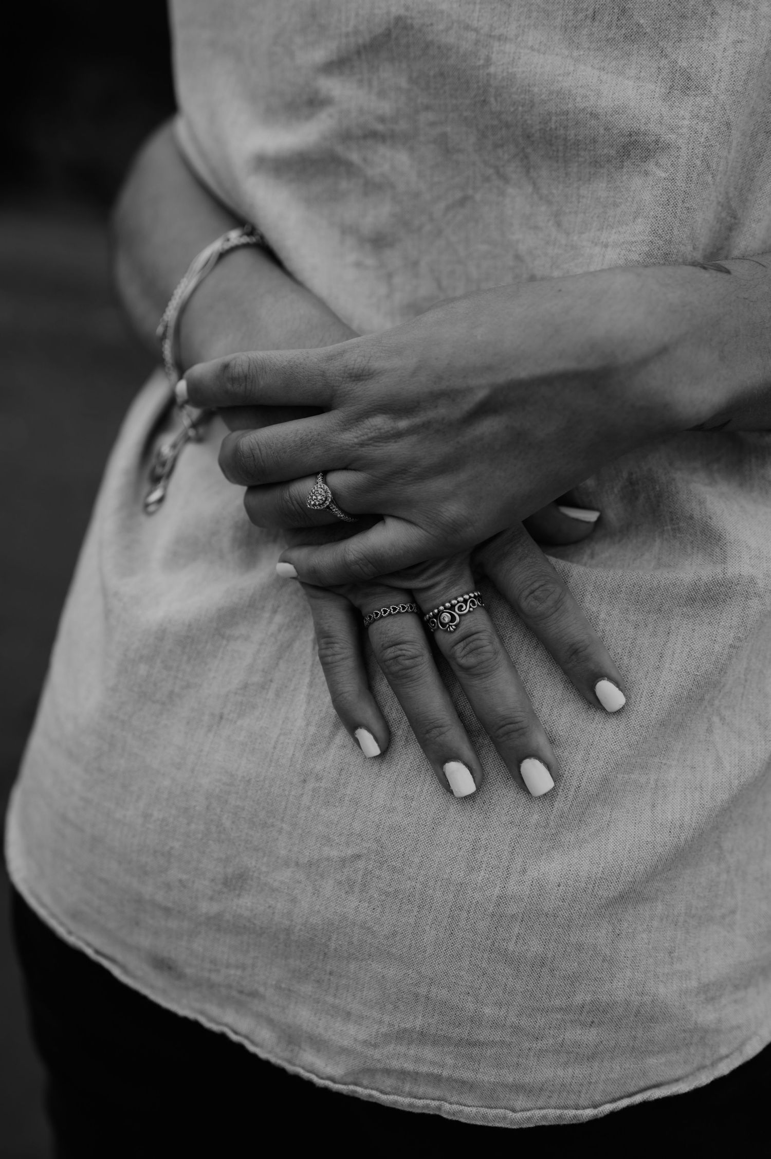Womans hands holding onto her fiances back in black and white for their Engagement shoot.