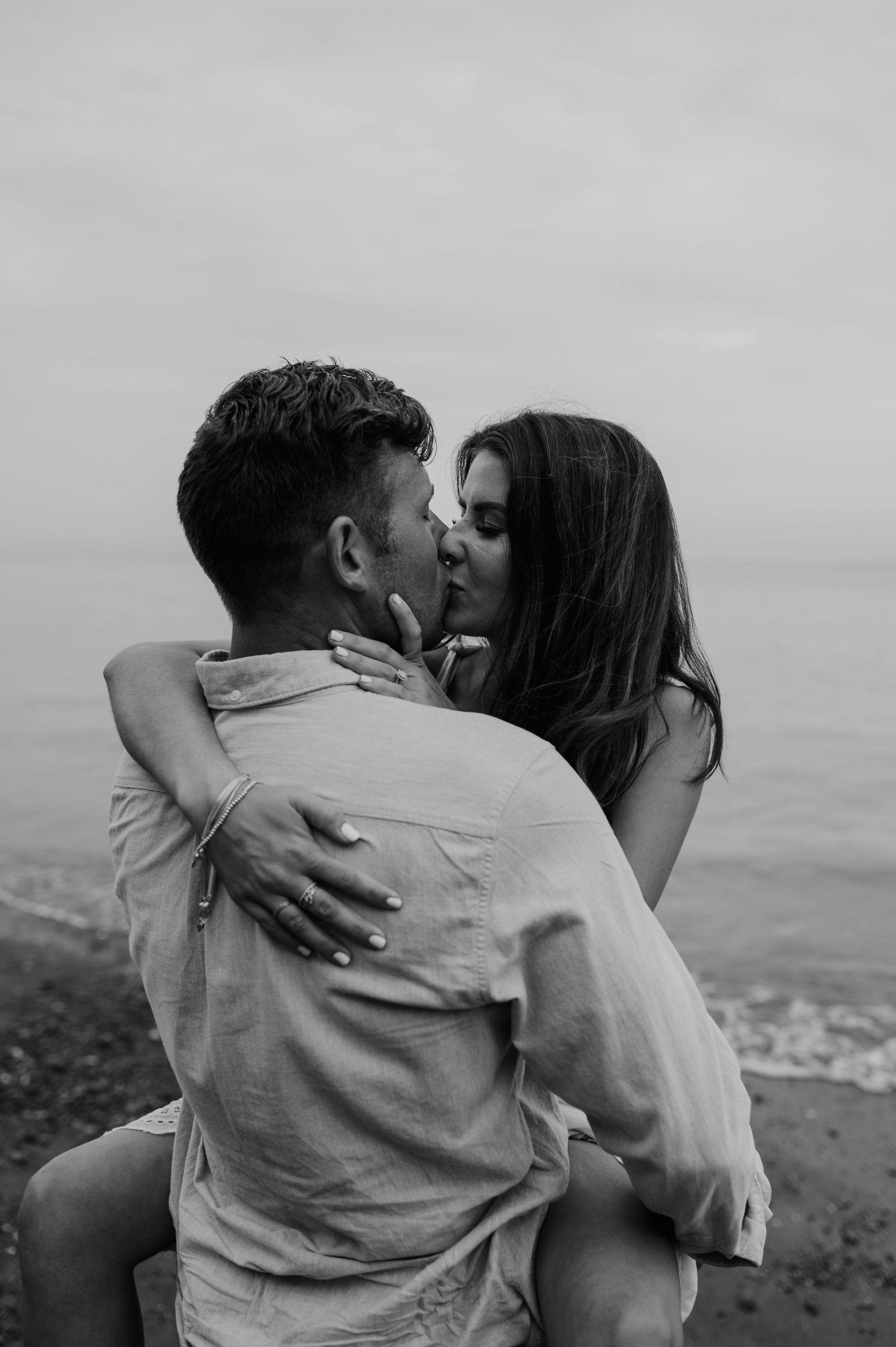 Couple embracing in a cuddle and romantic kiss on the beach for an engagement shoot.