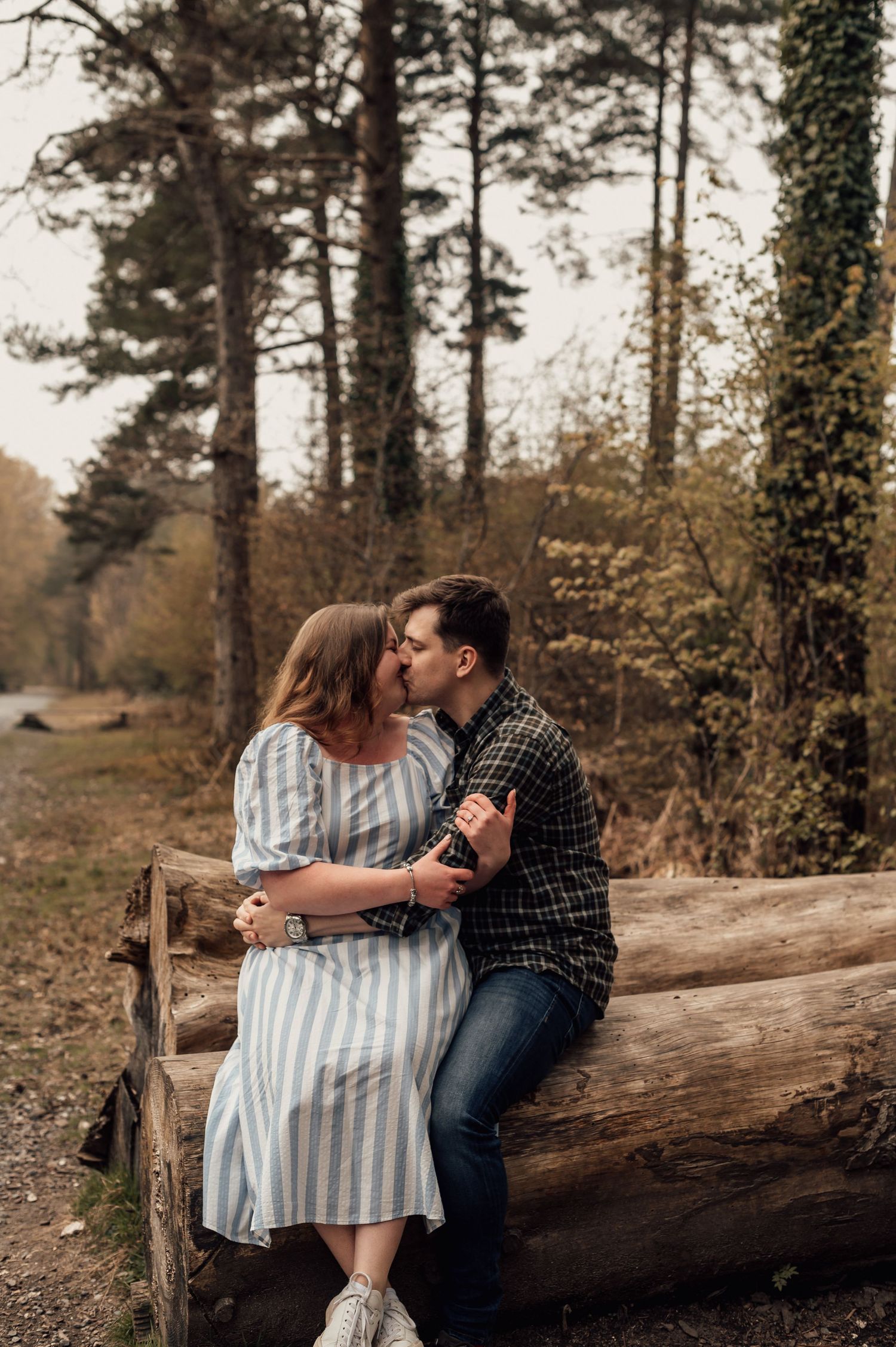 romantic couple sat on a log kissing in the woods at their couples engagement shoot in Haldon Forest.