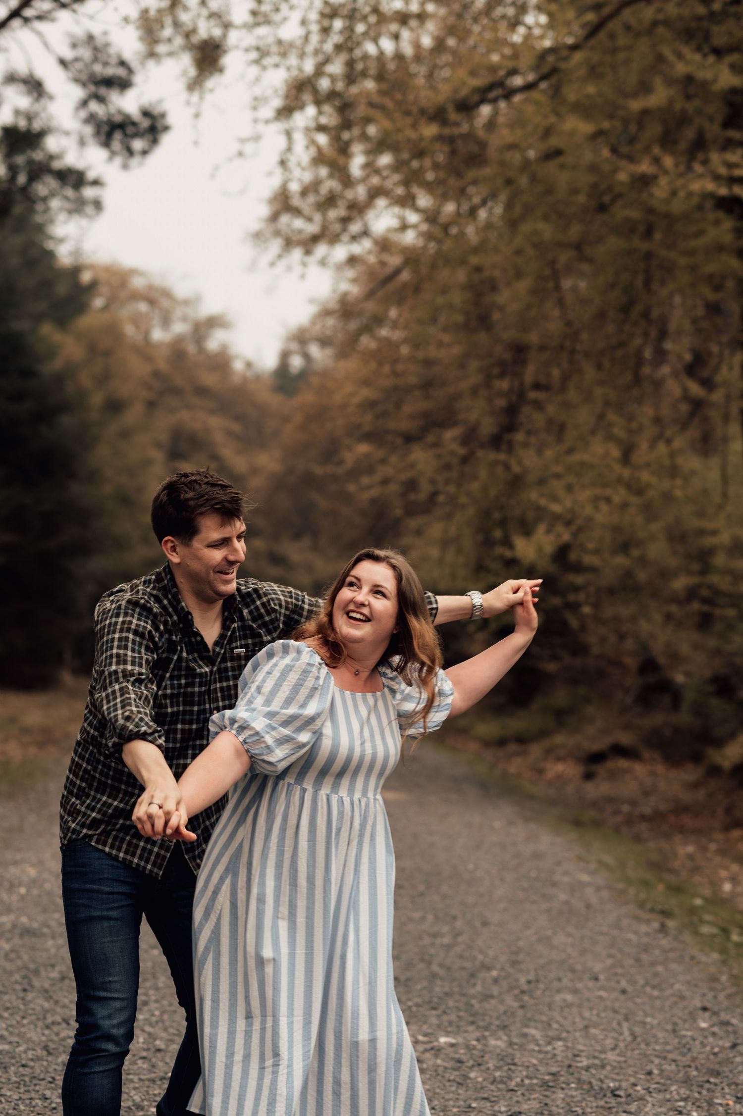 A couple laughs together while walking on a gravel path surrounded by autumn trees at Haldon Forest.