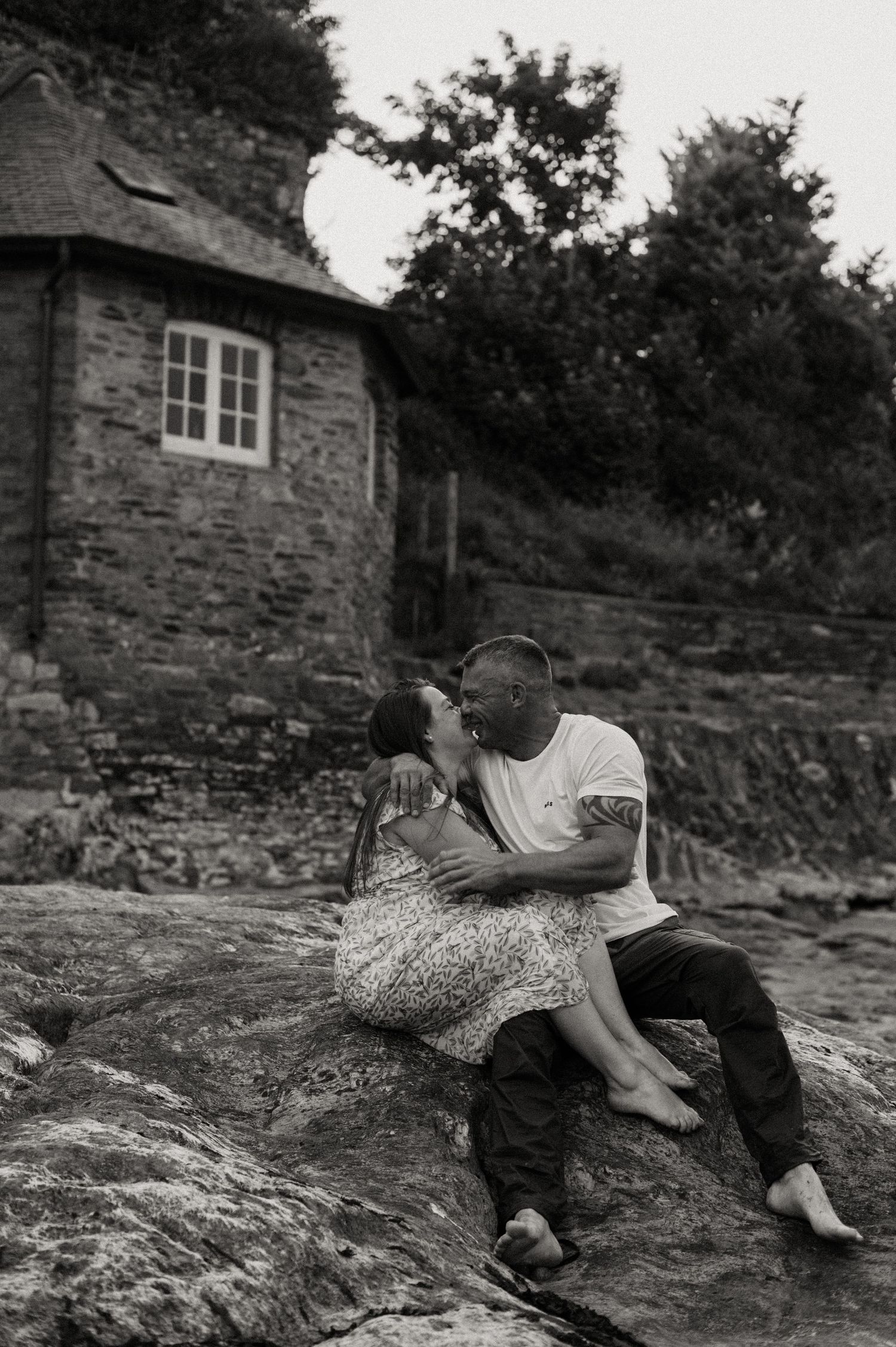 Mothecombe Beach engagement shoot with couple sat kissing on the rocks