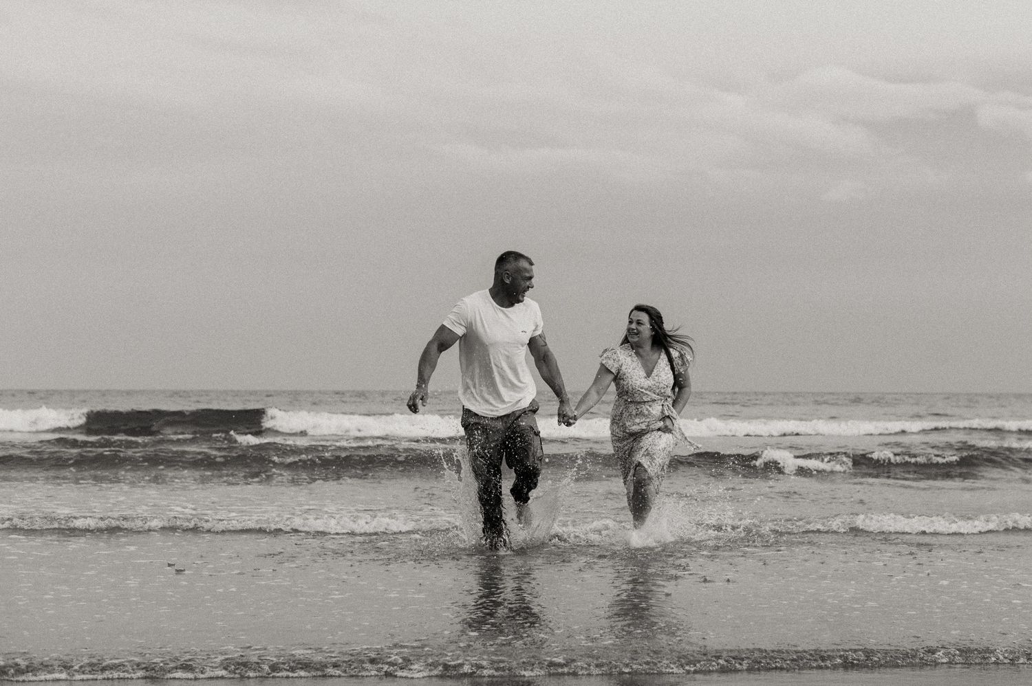 Excited couple running in the sea at Mothecombe Beach for their couples photoshoot