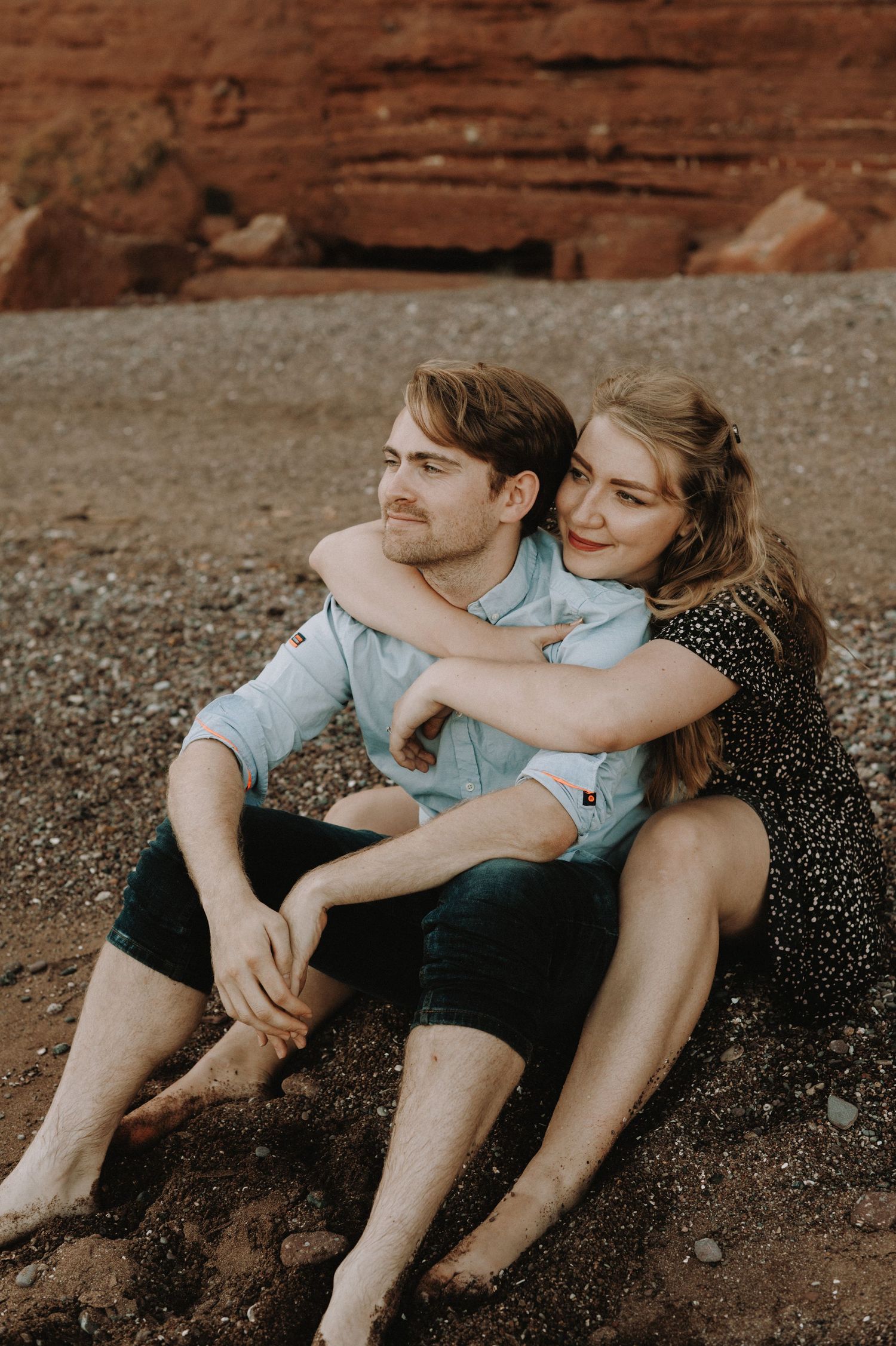 Happy couple having a cuddle sat on Teignmouth beach for their engagement shoot
