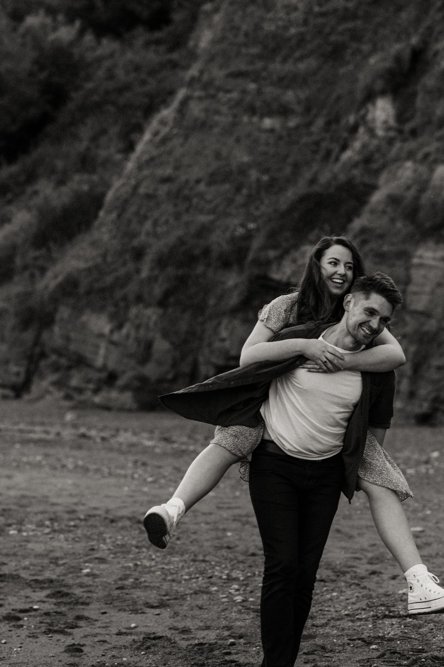 Happy couple piggybacking on the beach at their Teignmouth engagement shoot