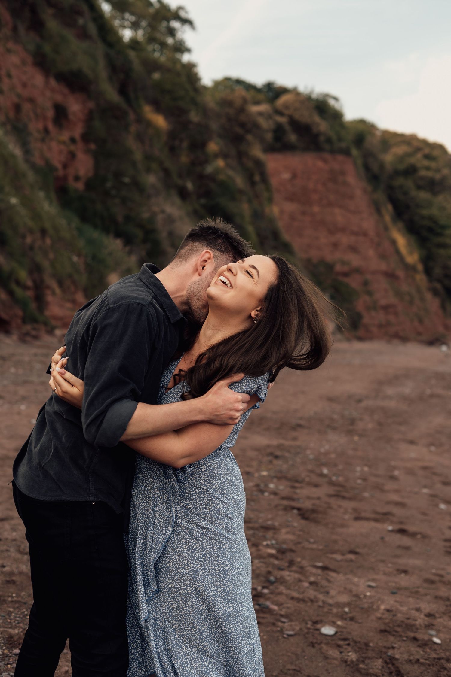 Fiance kissing his girlfriend on the neck playfully at Shaldon Beach for their couples photoshoot