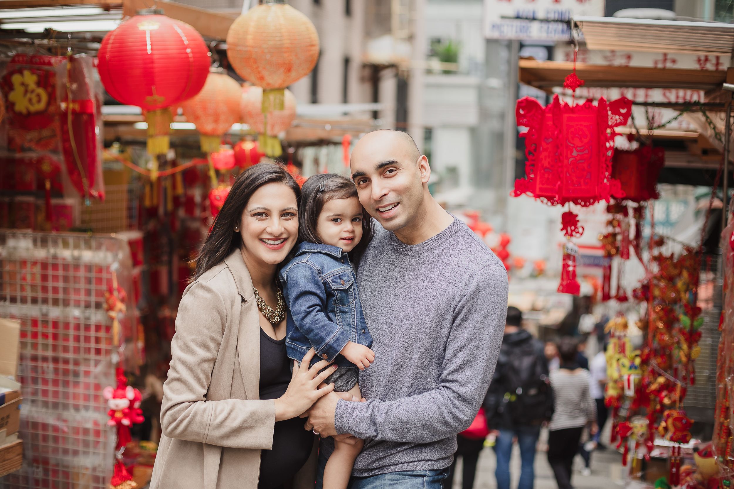 A family poses together in a street with traditional red Chinese lanterns and decorations.