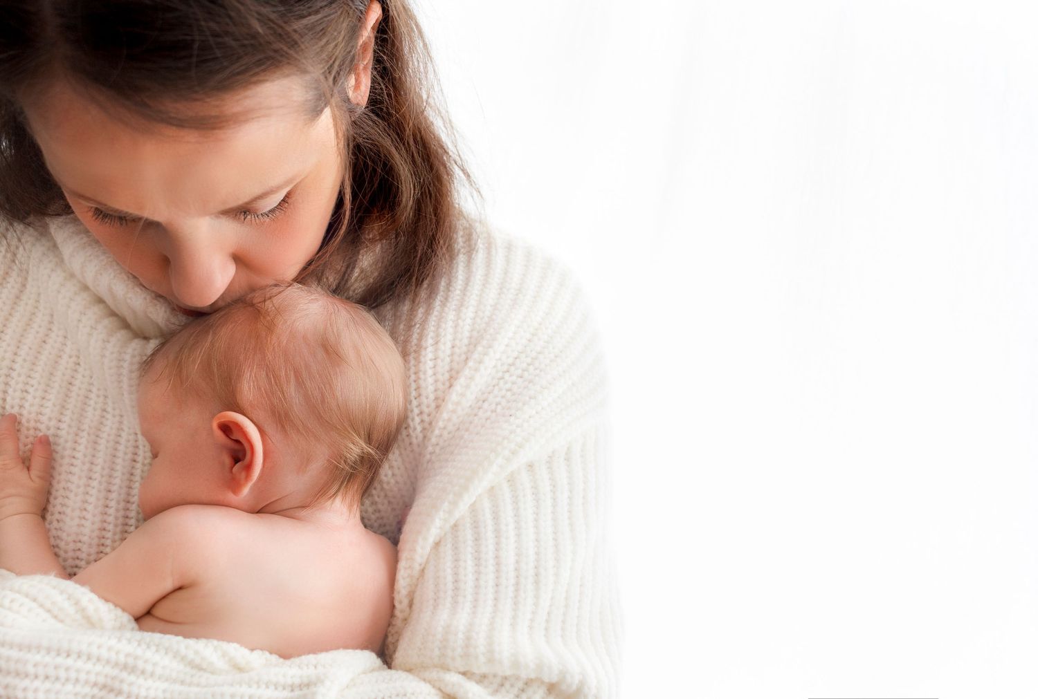 baby girl snuggles in as her mom kisses the top of her tiny head