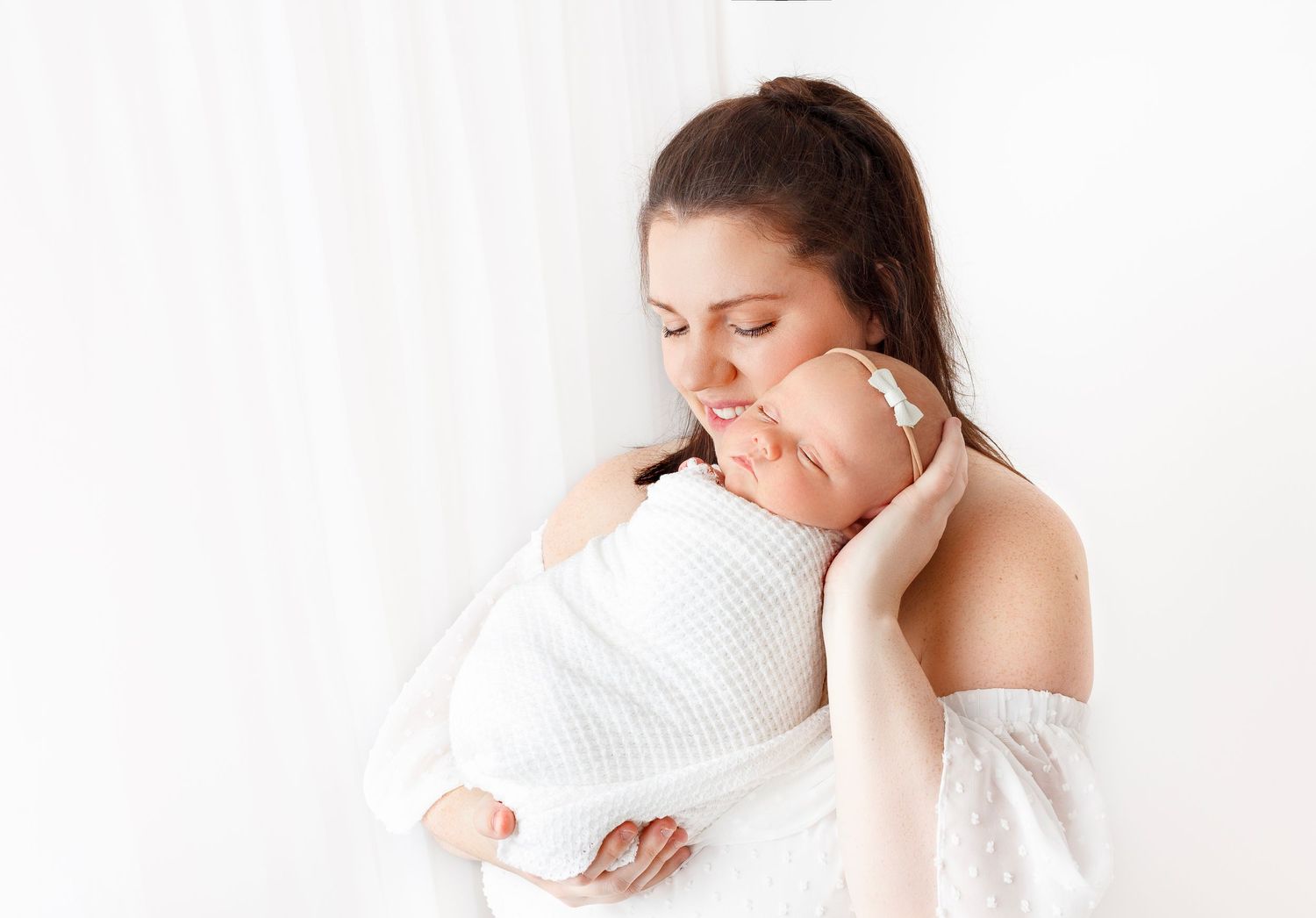 mother poses with her newborn during photo session in timeless white studio