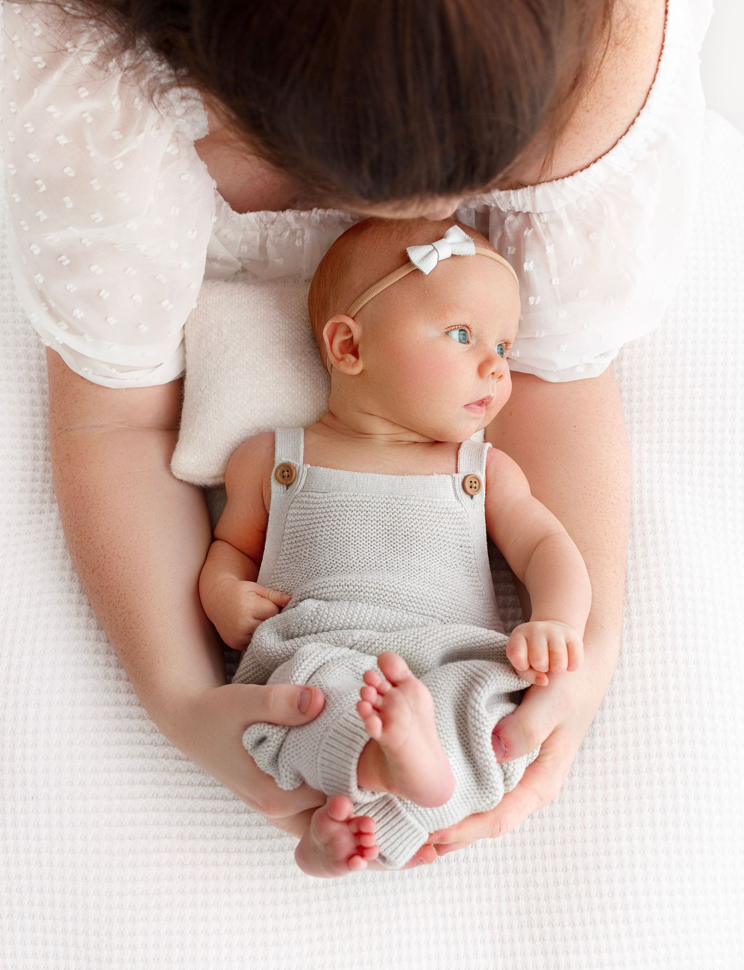 Mom looking down at her newborn with love as baby gazes quietly towards the light