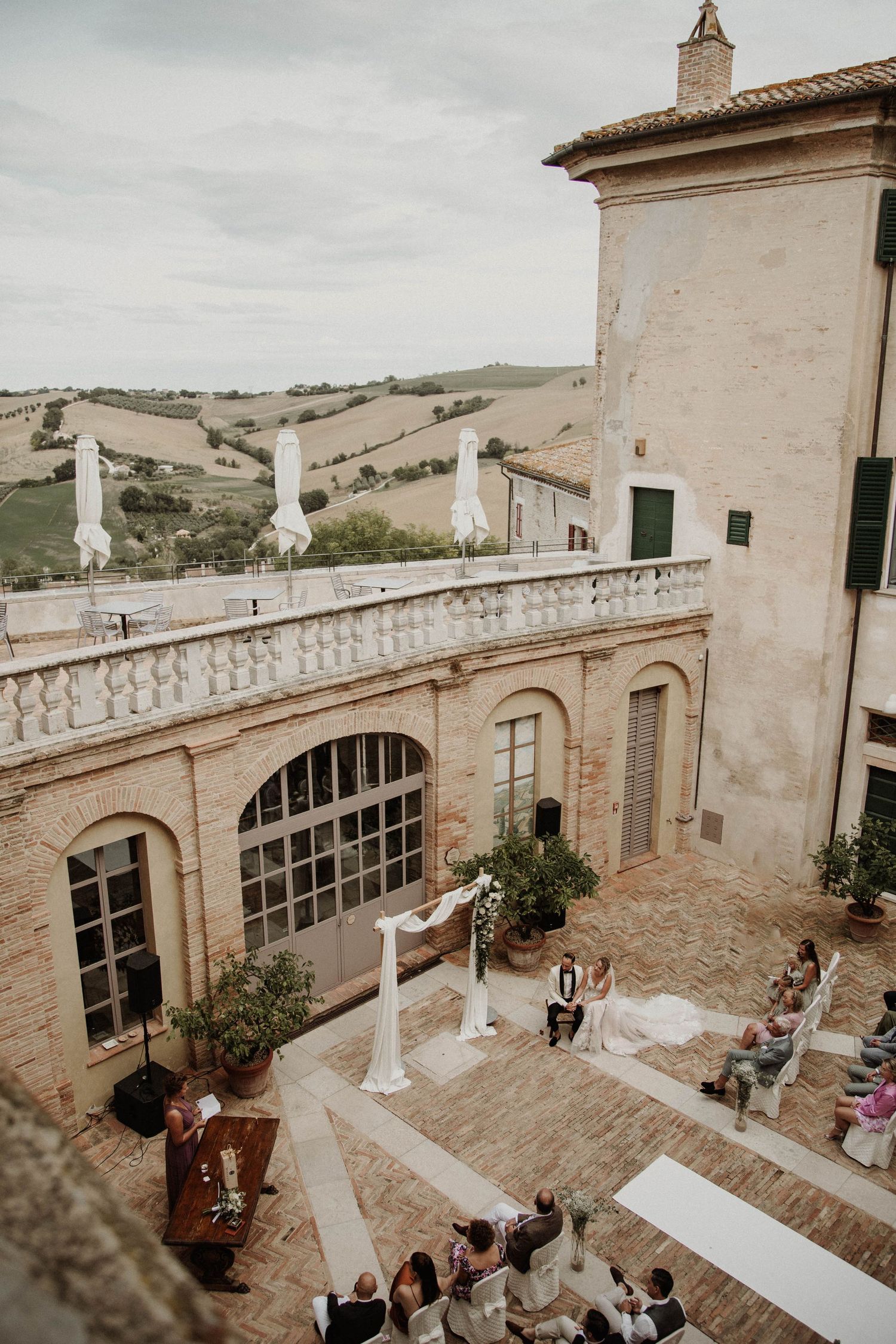 A wedding ceremony setup on an Italian villa terrace overlooking rolling countryside hills.
