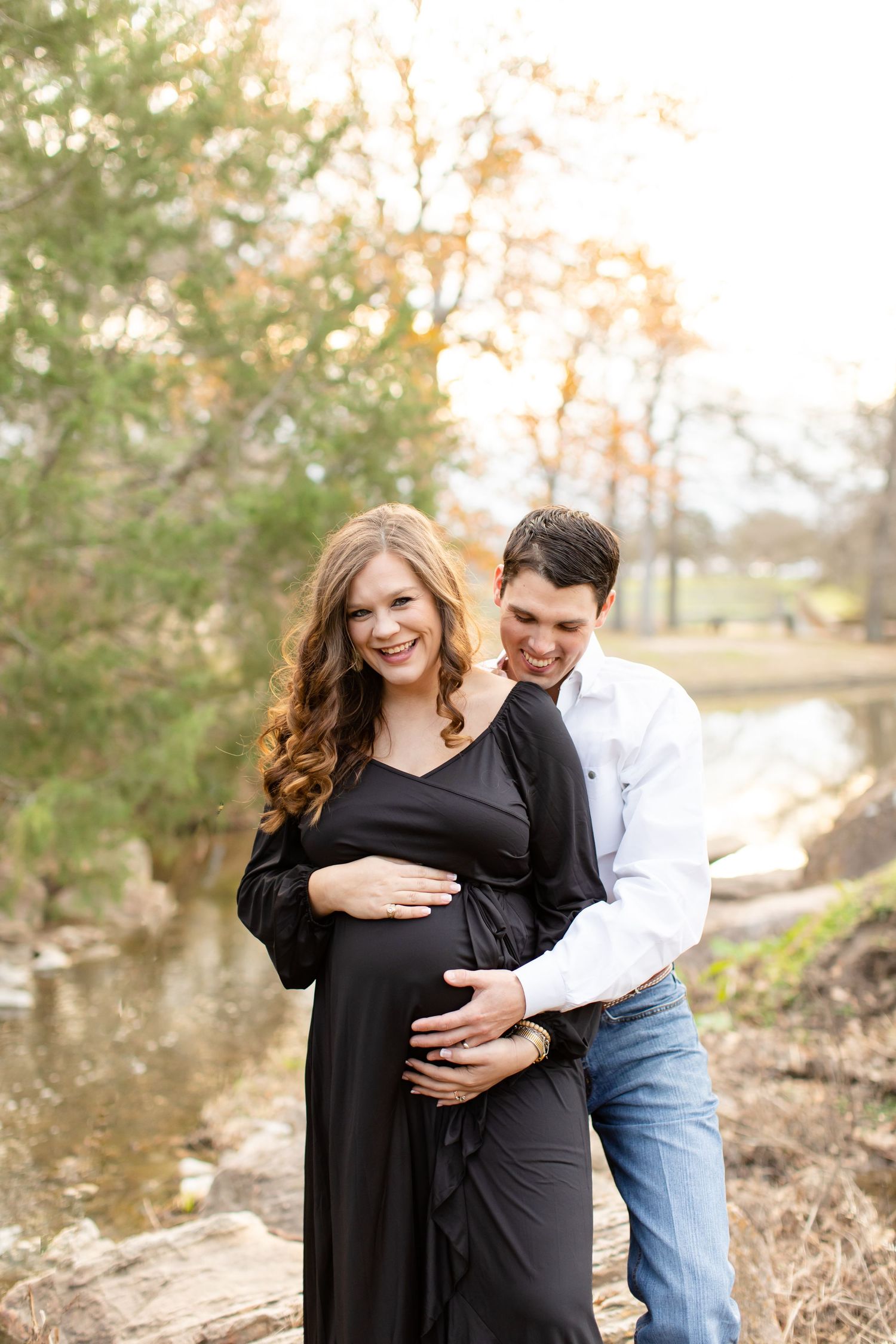 Romantic maternity photo by creek with couple in black dress and casual attire.
