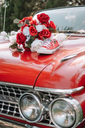 Red and white roses with vintage sneakers on classic red car hood.