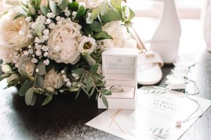 Wedding details featuring white floral bouquet, invitation cards and ring box in soft natural light.